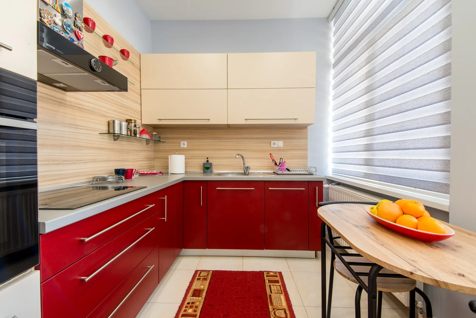 dapur kecil bentuk L dengan kabinet merah dan meja makan kayu