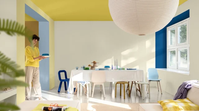 ruang tamu dengan warna cat biru, kuning, dan putih serta sofa krem
