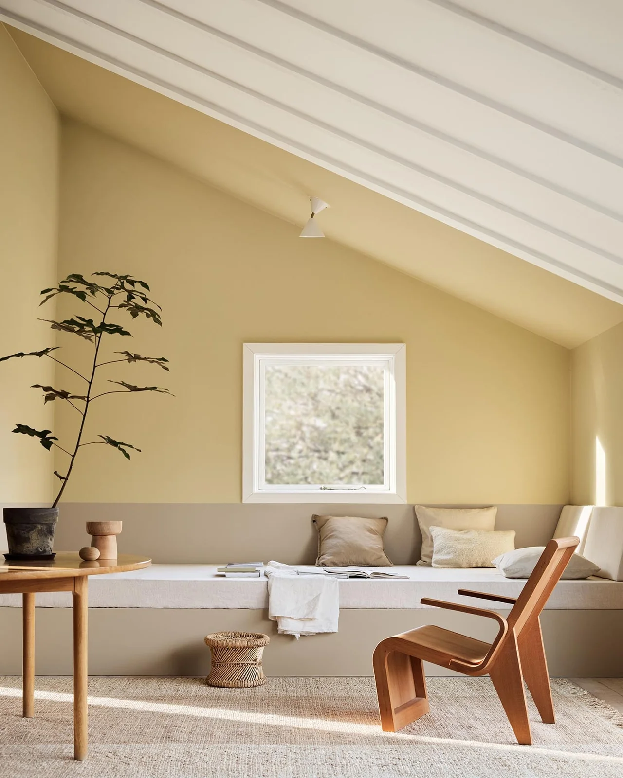 ruang duduk dengan dinding beige keemasan, daybed, dan kursi kayu