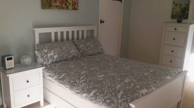 kamar tidur dengan ranjang putih berlaci di bawah kasur dan nakas