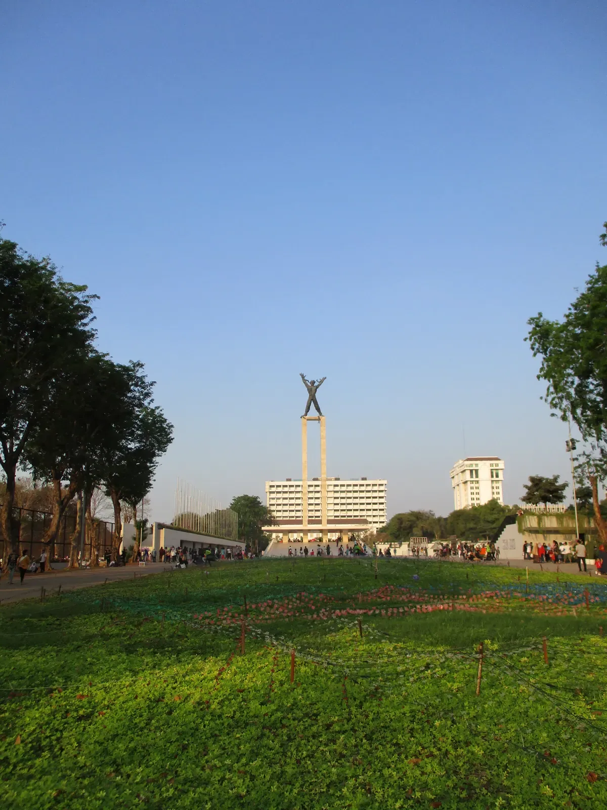 tugu tinggi dengan patung pria memutus rantai di tengah taman Lapangan Banteng