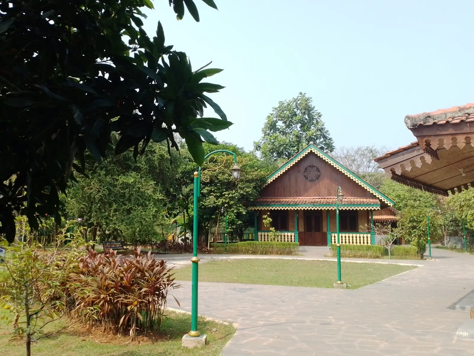 rumah kayu Betawi beratap genteng dengan teras terbuka di tengah pepohonan