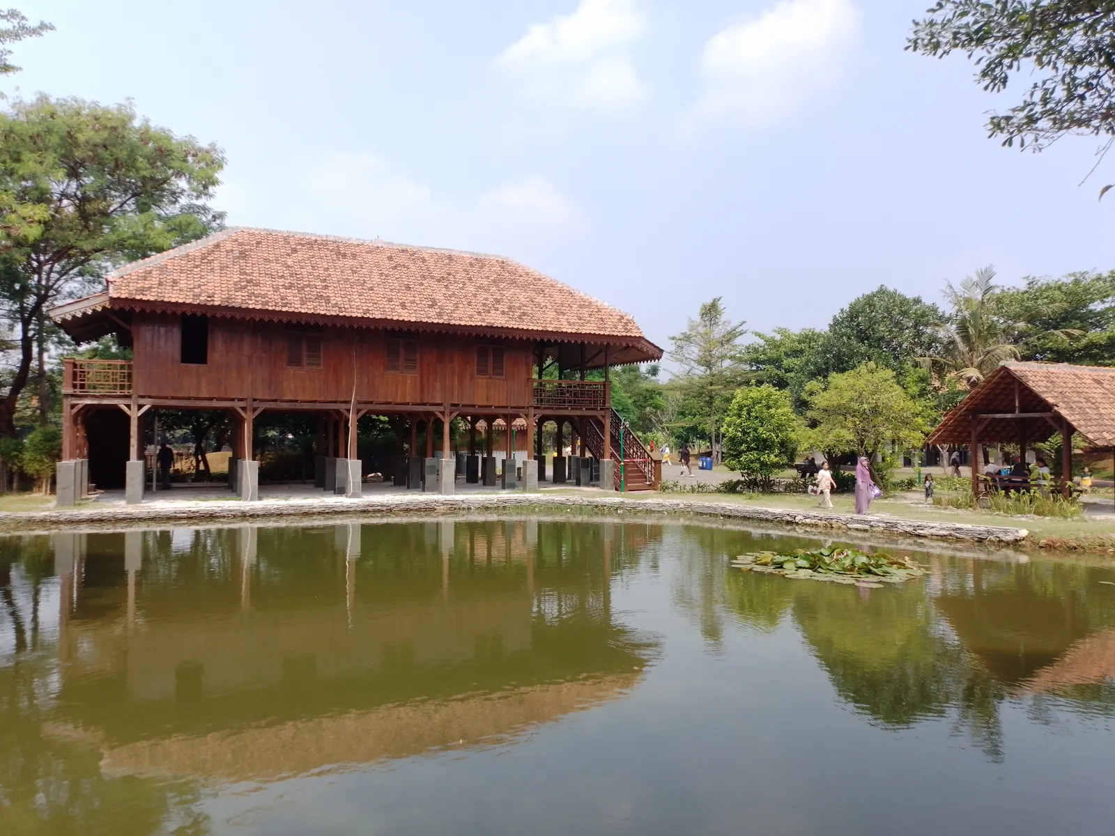 rumah panggung kayu beratap genteng lebar di tepi kolam