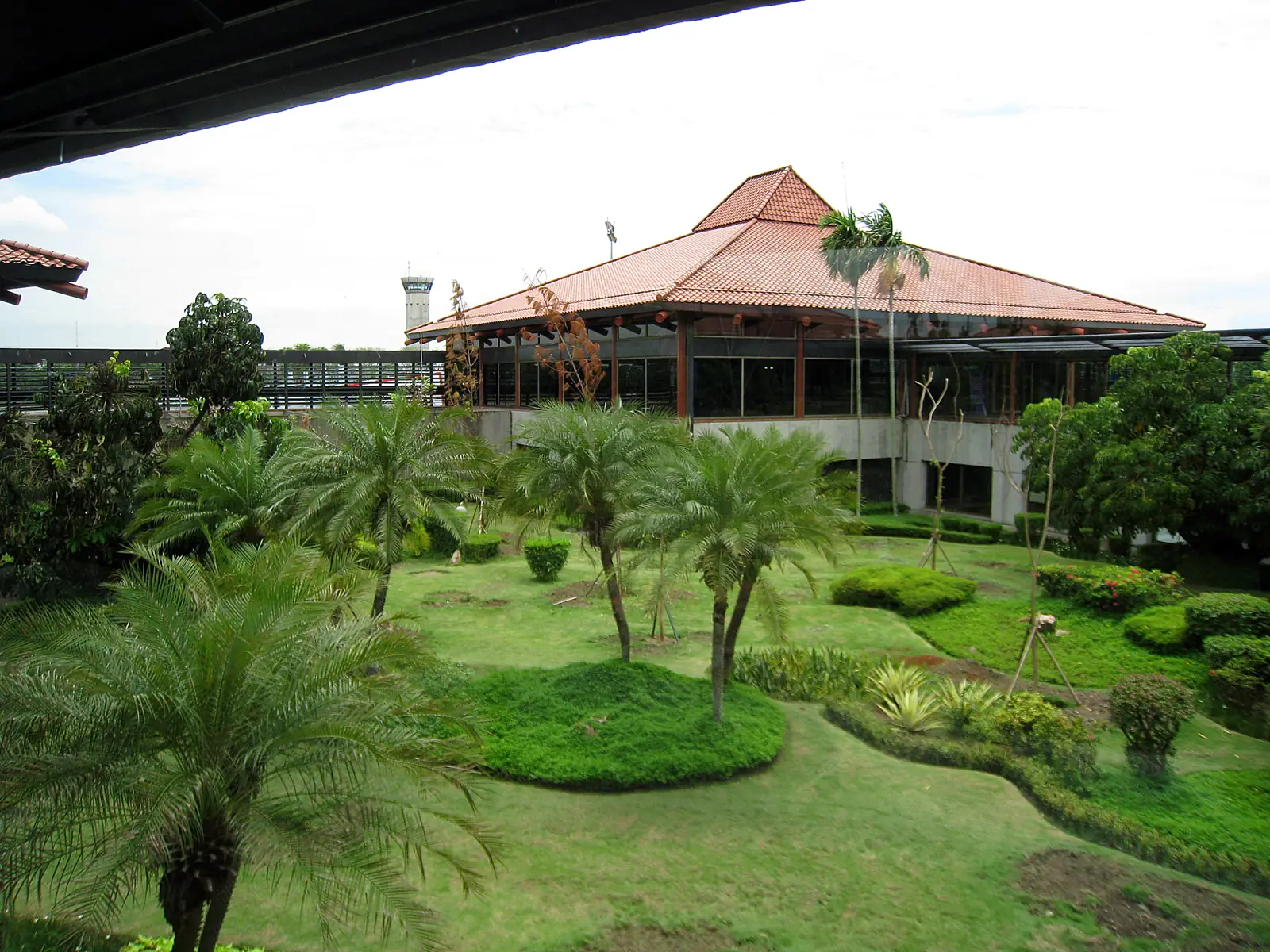 taman tropis dengan pohon palem di depan paviliun beratap genteng Terminal 2 Soekarno-Hatta