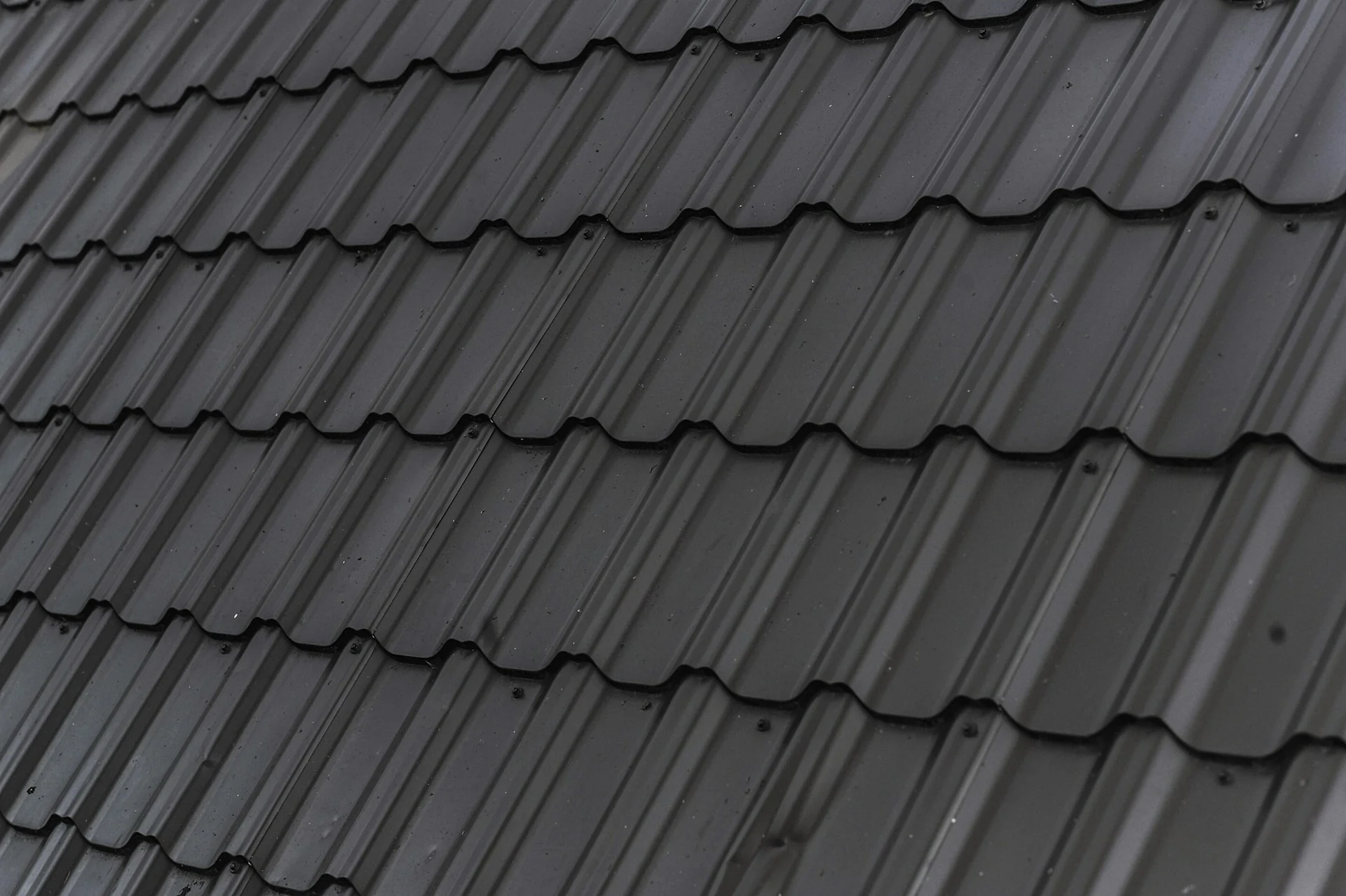Atap rumah berlapis genteng metal hitam bermotif gelombang yang tersusun rapi