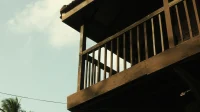 Lantai atas rumah dari kayu dengan balkon pagar kayu di antara pohon kelapa
