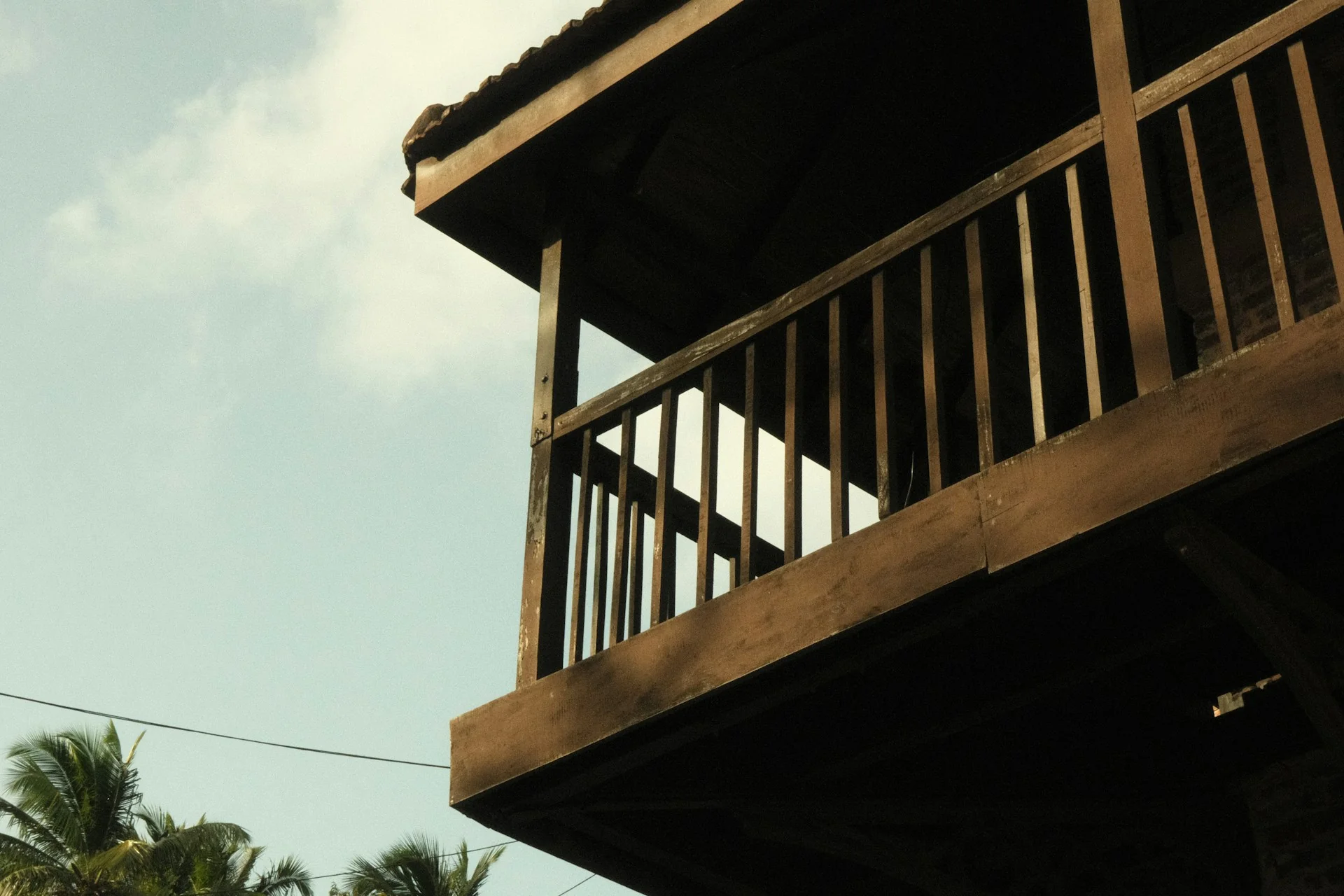 Balkon kayu lantai atas rumah tropis Lantai atas rumah dari kayu dengan balkon pagar kayu di antara pohon kelapa