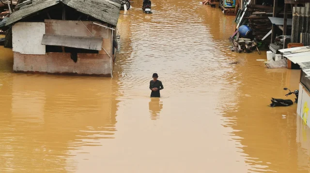 Warga berdiri di genangan banjir di antara rumah permukiman Rawa Jati, gambaran mengapa rumah anti banjir Jakarta dibutuhkan