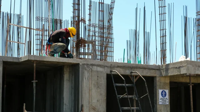 pekerja di atas balok beton lantai yang sudah dicor dengan rangkaian besi tulangan dan sengkang kolom menjulang di atasnya