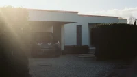 Carport minimalis beratap datar menyatu dengan rumah modern putih, mobil terparkir di bawahnya