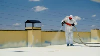 coating-waterproofing-dak-beton Pekerja berbaju pelindung menyemprotkan coating waterproofing putih di dak beton atap datar