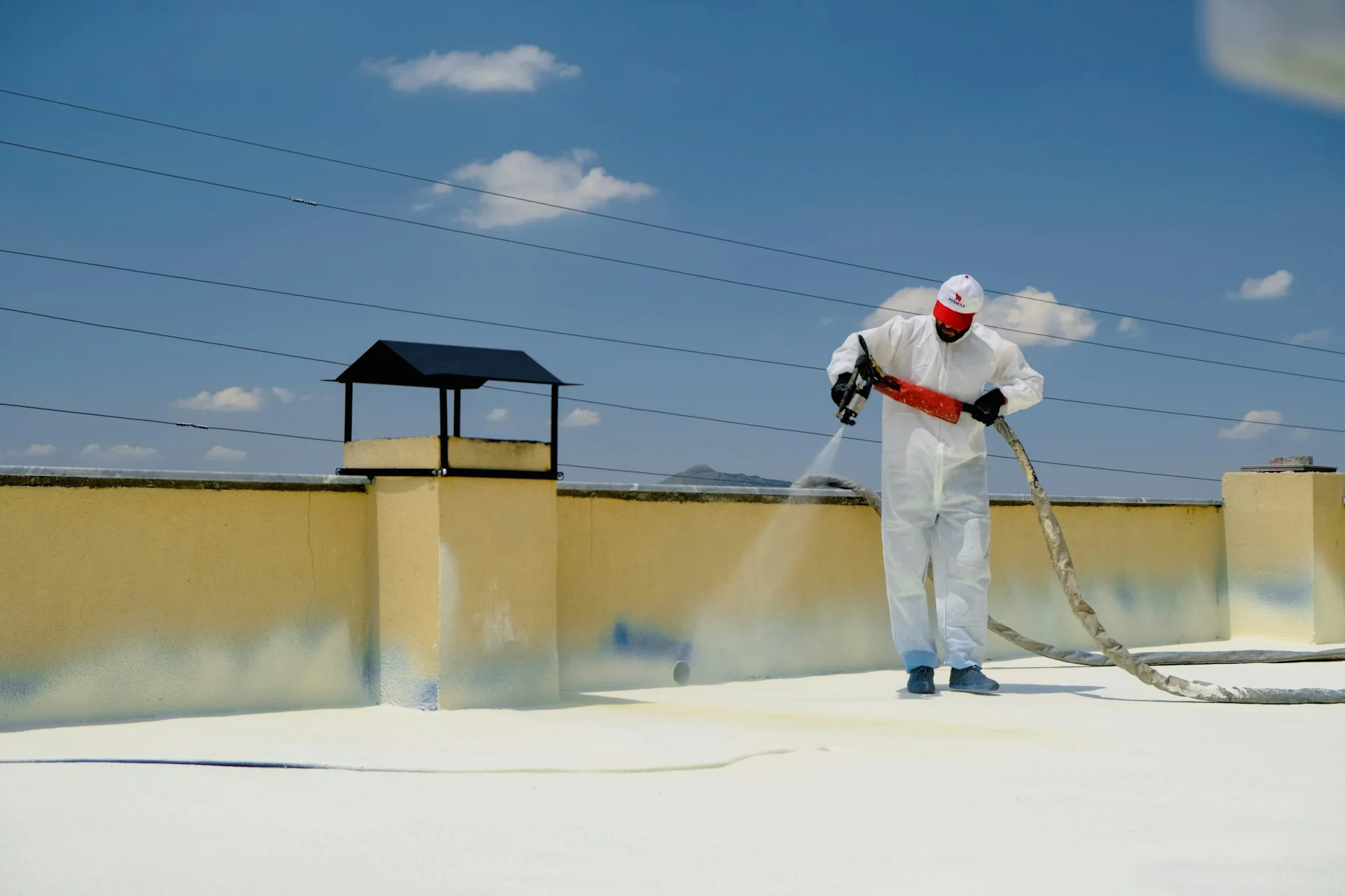 Pekerja berbaju pelindung menyemprotkan coating waterproofing putih di dak beton atap datar