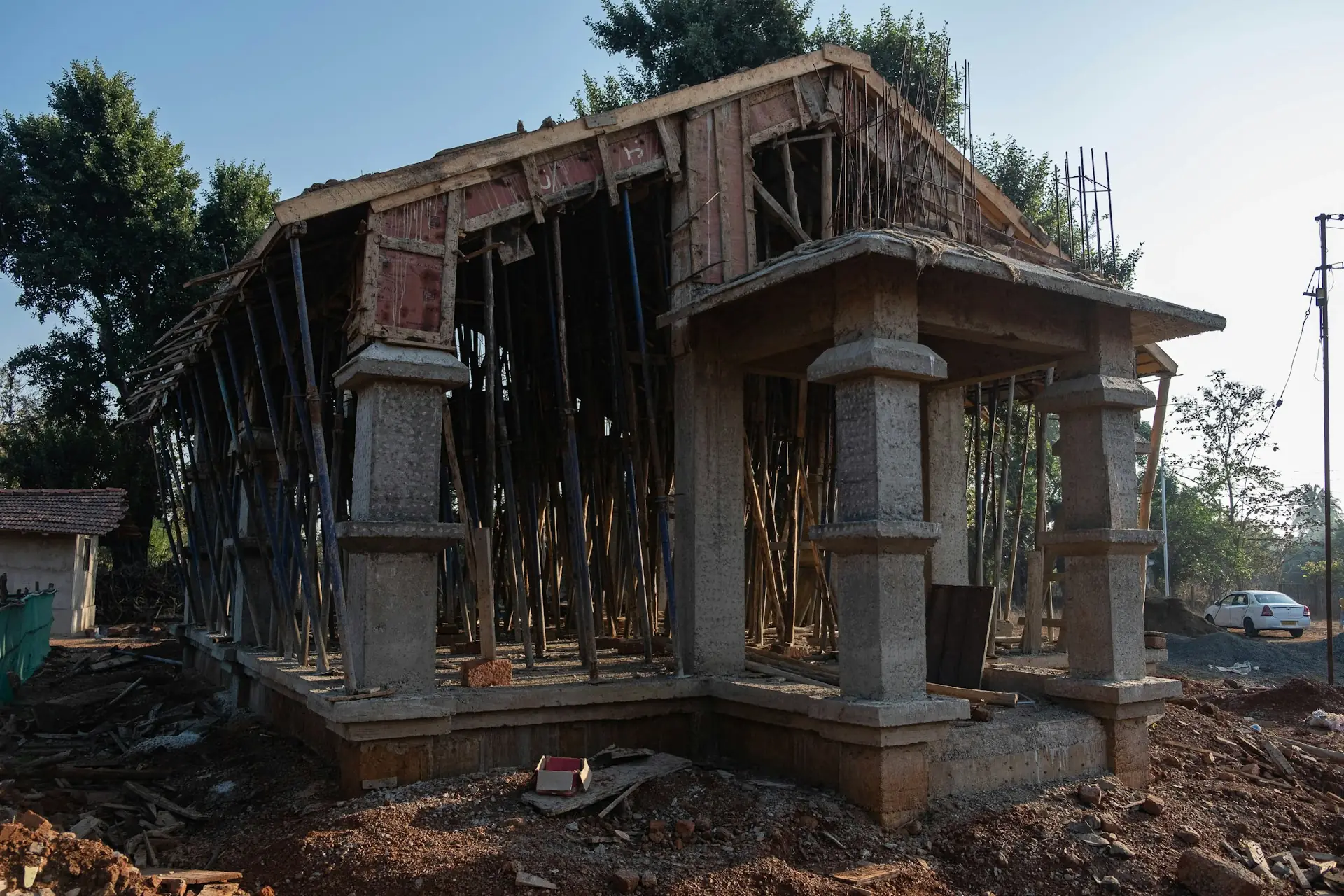 rumah yang sedang dibangun dengan kolom beton, pelat dak ditopang tiang penyangga, dan stek besi kolom