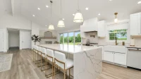 Dapur bersih modern dengan kitchen island marmer putih, kursi bar, dan kabinet putih