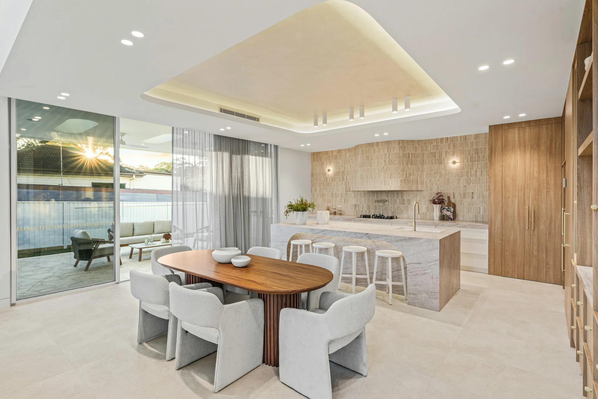 Meja makan kayu oval menyatu dengan kitchen island batu dan pantry di ruang terbuka