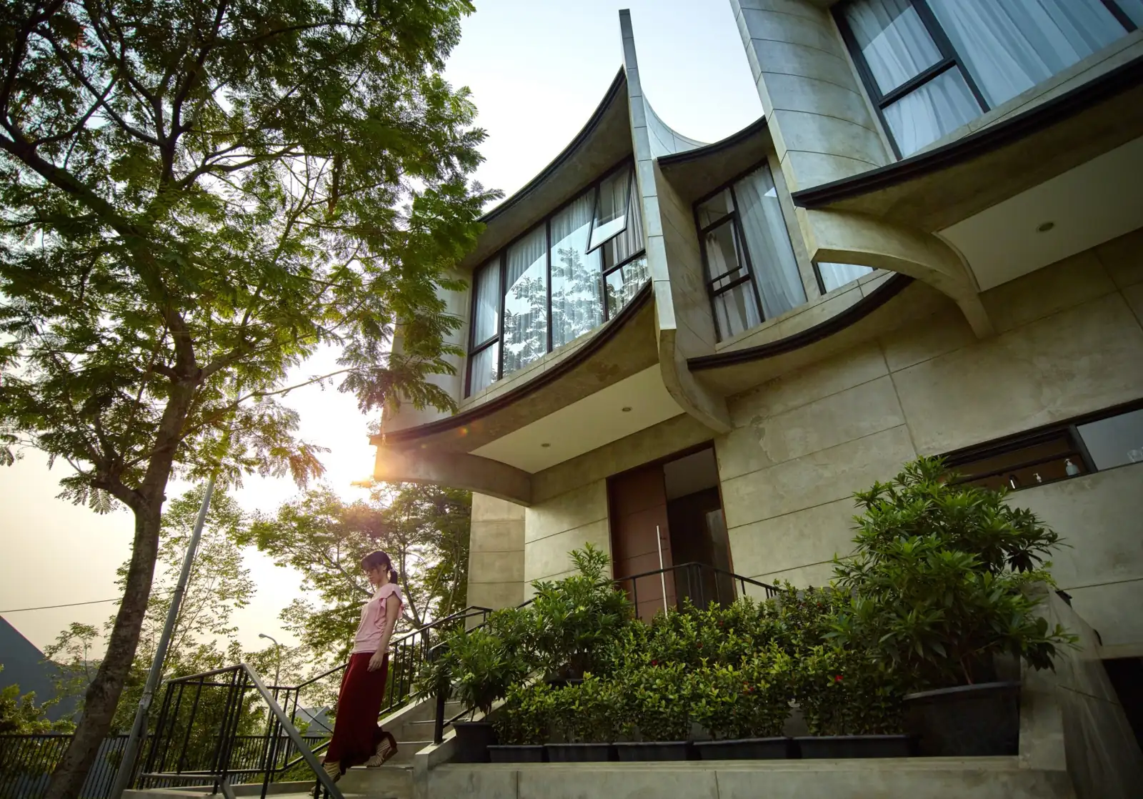 desain rumah tropis Kampono House dengan sirip beton melengkung di antara pepohonan