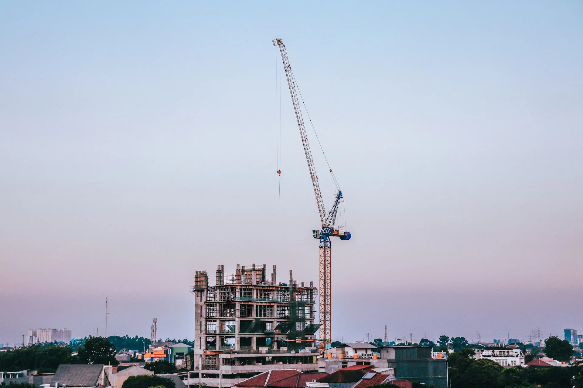 Gedung bertingkat yang masih berupa struktur beton dengan tower crane di sampingnya