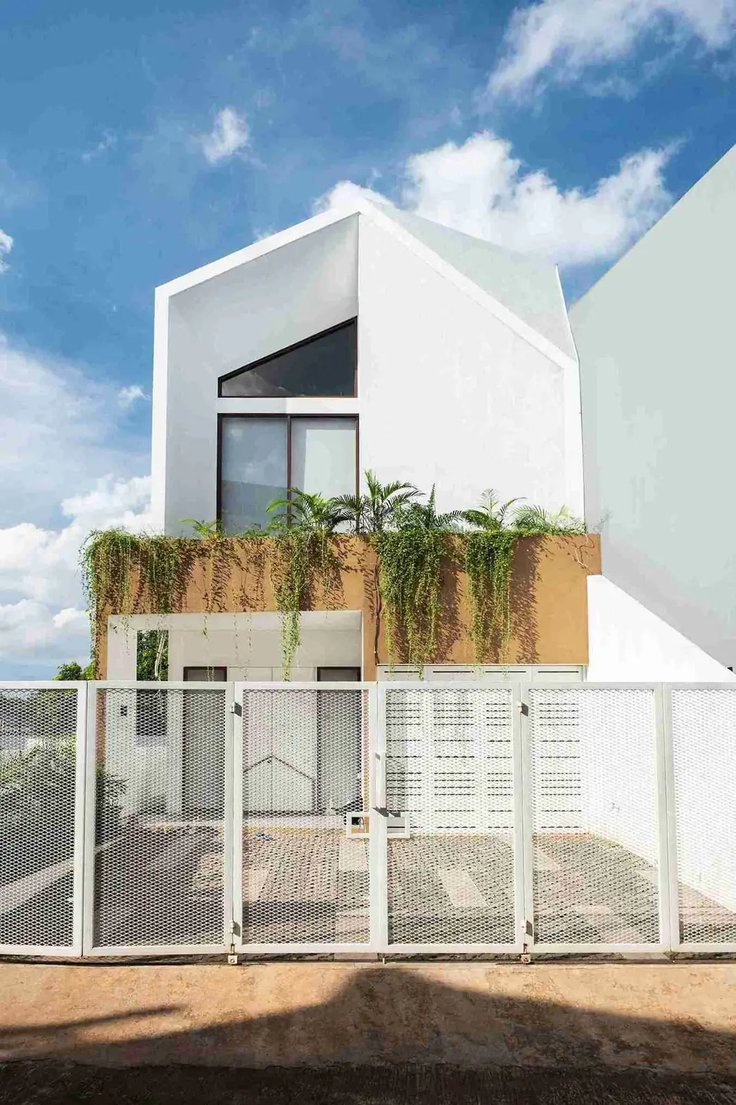 fasad GREID House putih dengan bukaan segitiga dan tanaman di balkon