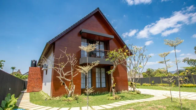 Halaman rumput rumah dengan jalur paving di depan rumah kayu