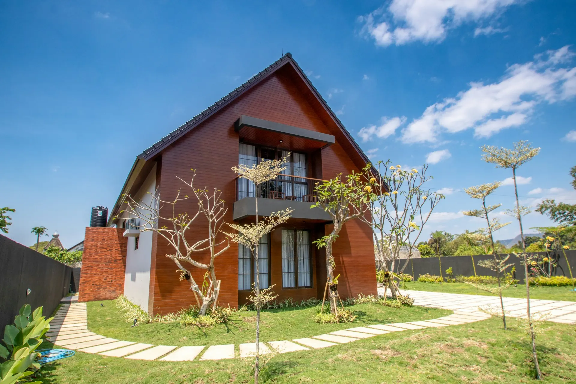 Halaman rumput rumah dengan jalur paving di depan rumah kayu