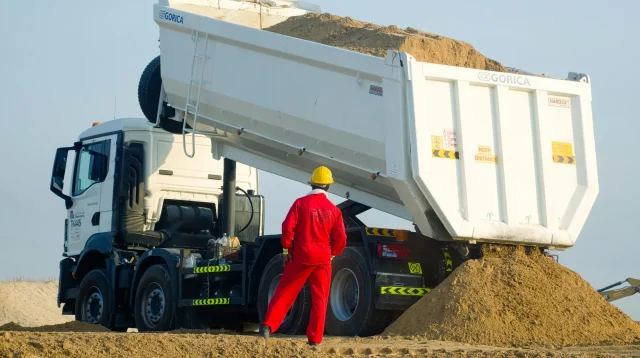 Dump truck menuang pasir di lokasi proyek dengan pekerja berhelm kuning mengawasi, gambaran pengiriman yang menentukan harga pasir per kubik