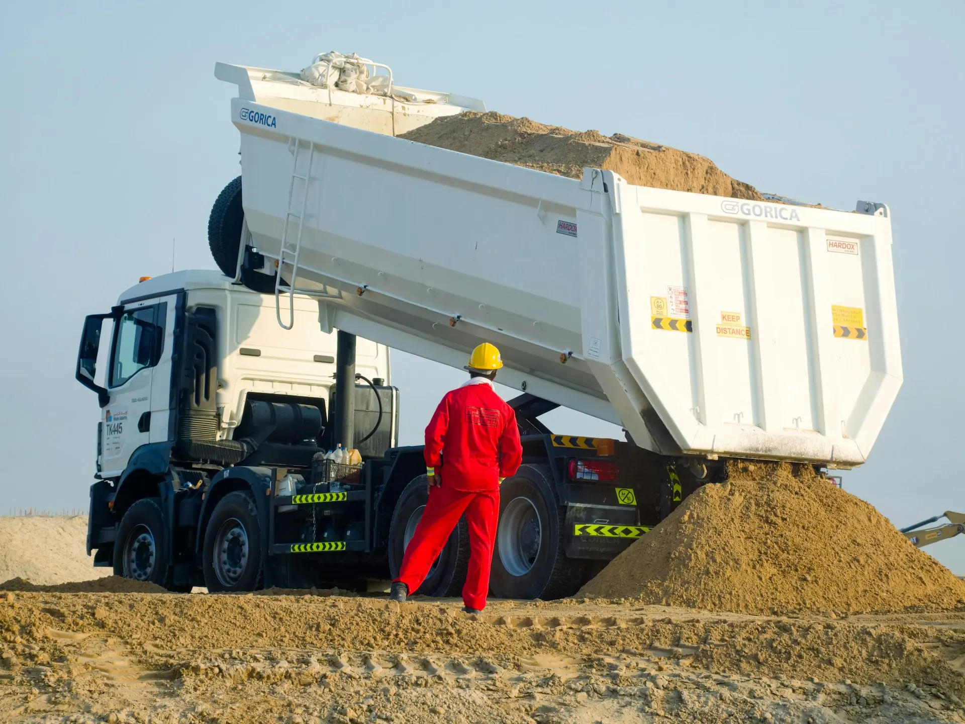 Dump truck menuang pasir di lokasi proyek dengan pekerja berhelm kuning mengawasi, gambaran pengiriman yang menentukan harga pasir per kubik