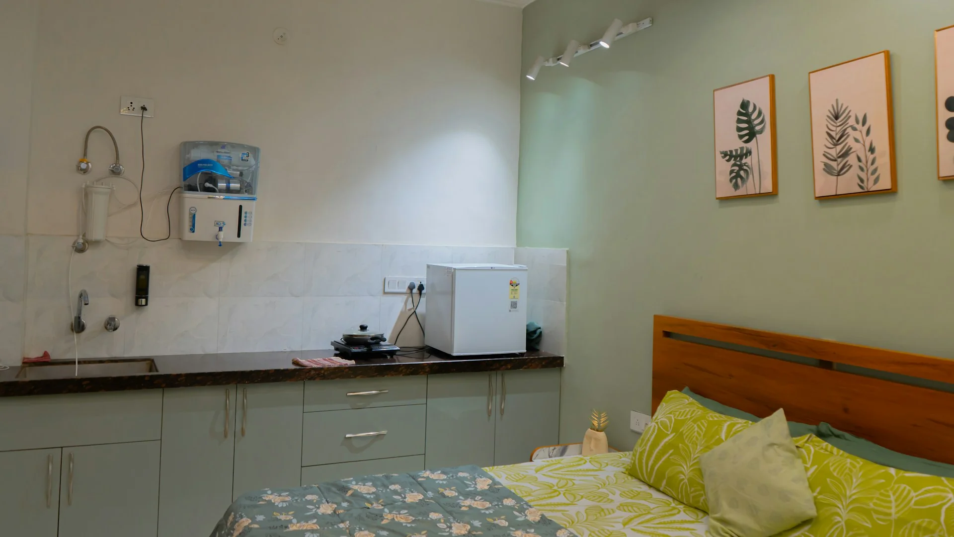 Interior unit apartemen studio dengan dapur kecil, kulkas mini, dan tempat tidur dalam satu ruang