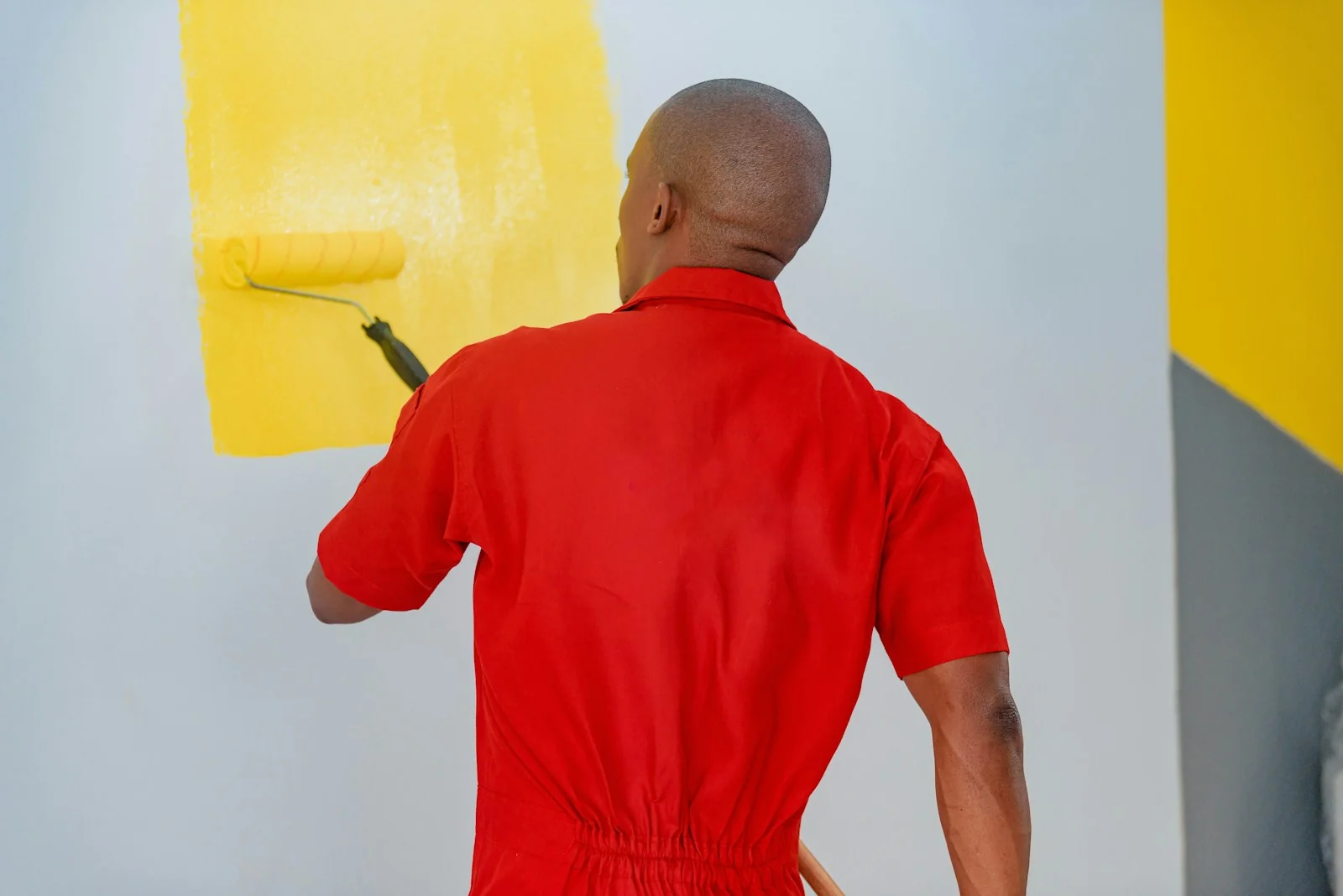 pekerja berbaju merah mengecat dinding putih dengan rol warna kuning