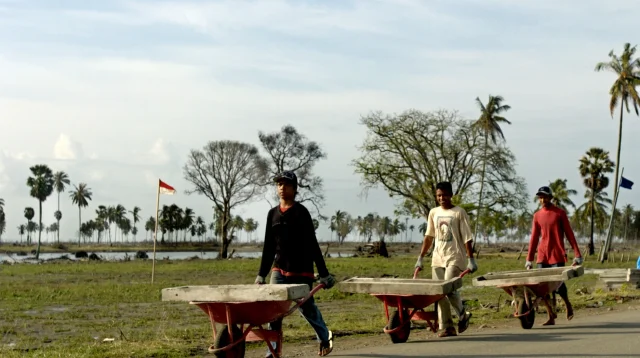 Tiga pekerja bangunan mendorong gerobak berisi panel beton untuk proyek rumah di Aceh