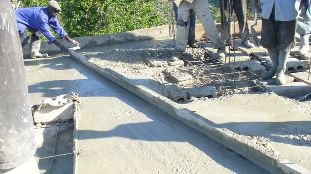Pekerja meratakan cor dak beton segar dengan papan di atas atap bangunan