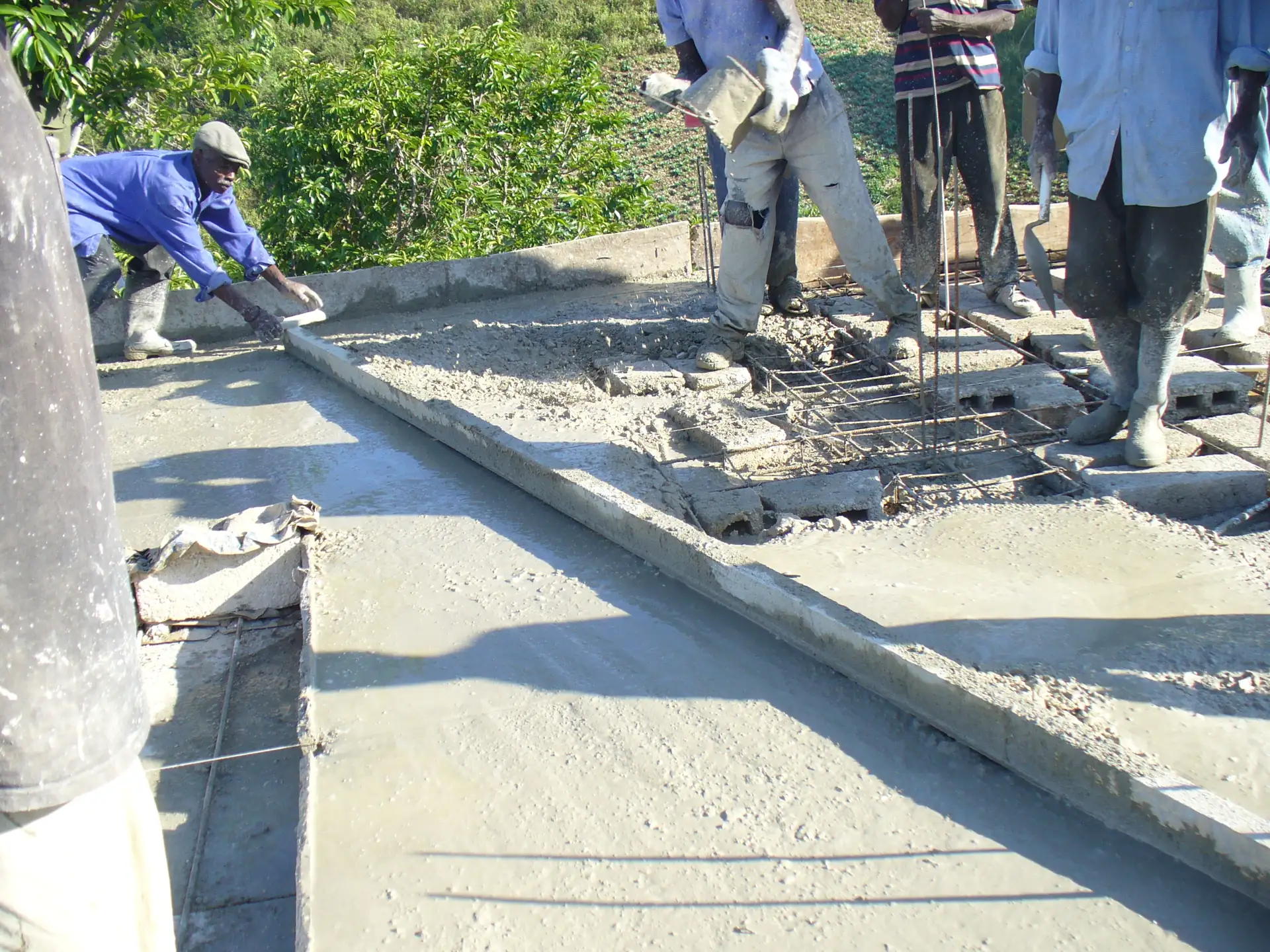 Pekerja meratakan cor dak beton segar dengan papan di atas atap bangunan