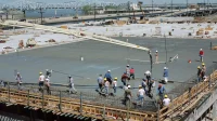 pekerja meratakan beton segar di atas pelat lantai bertulang, dengan pipa pompa beton menuangkan adukan
