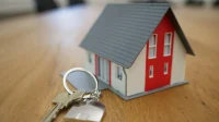 Miniatur rumah dan kunci di atas meja kayu