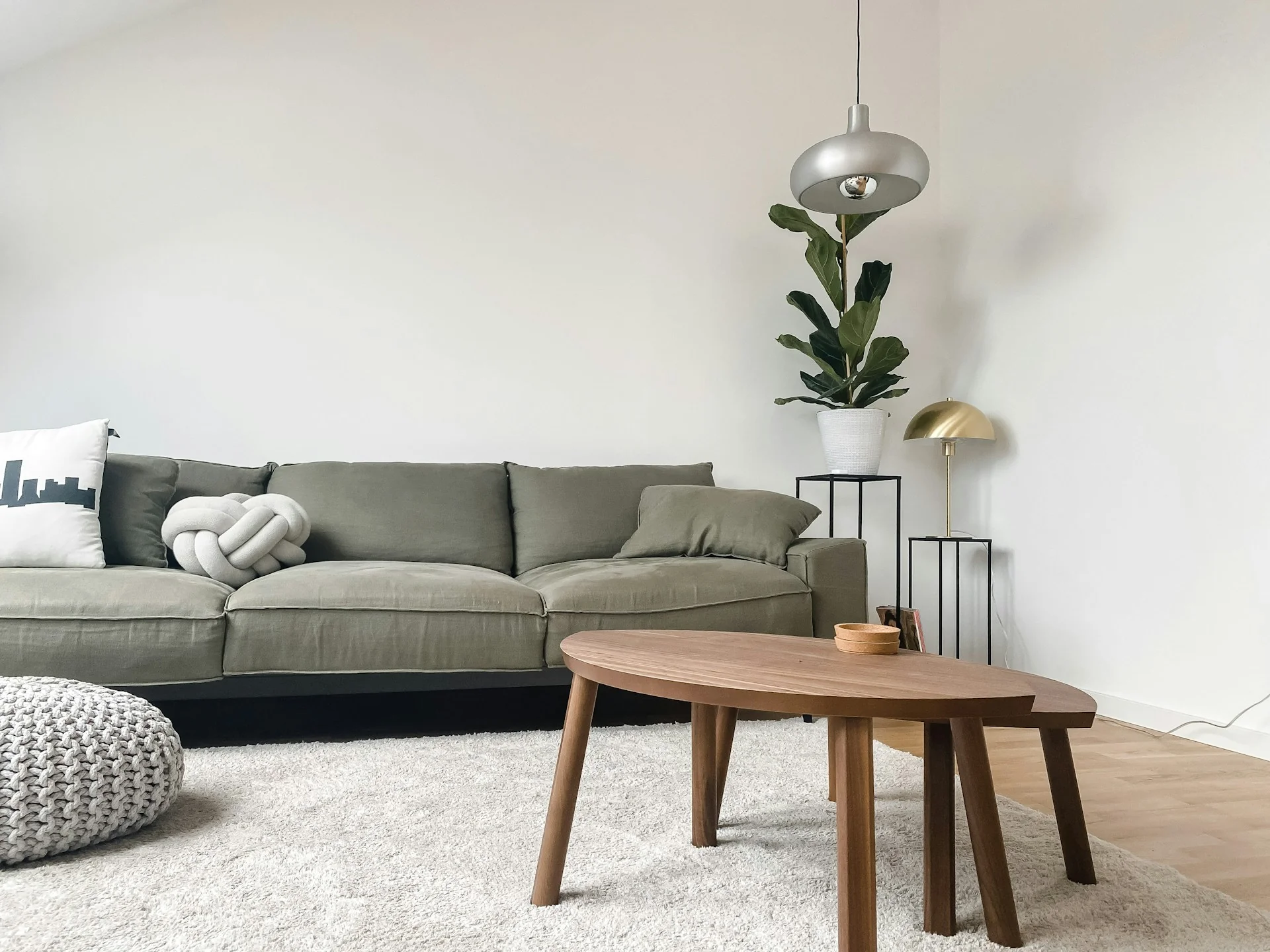 ruang-tamu-rumah-japandi-sofa-rendah Ruang tamu rumah japandi dengan sofa rendah hijau zaitun, meja kopi kayu, karpet krem, dan tanaman pot