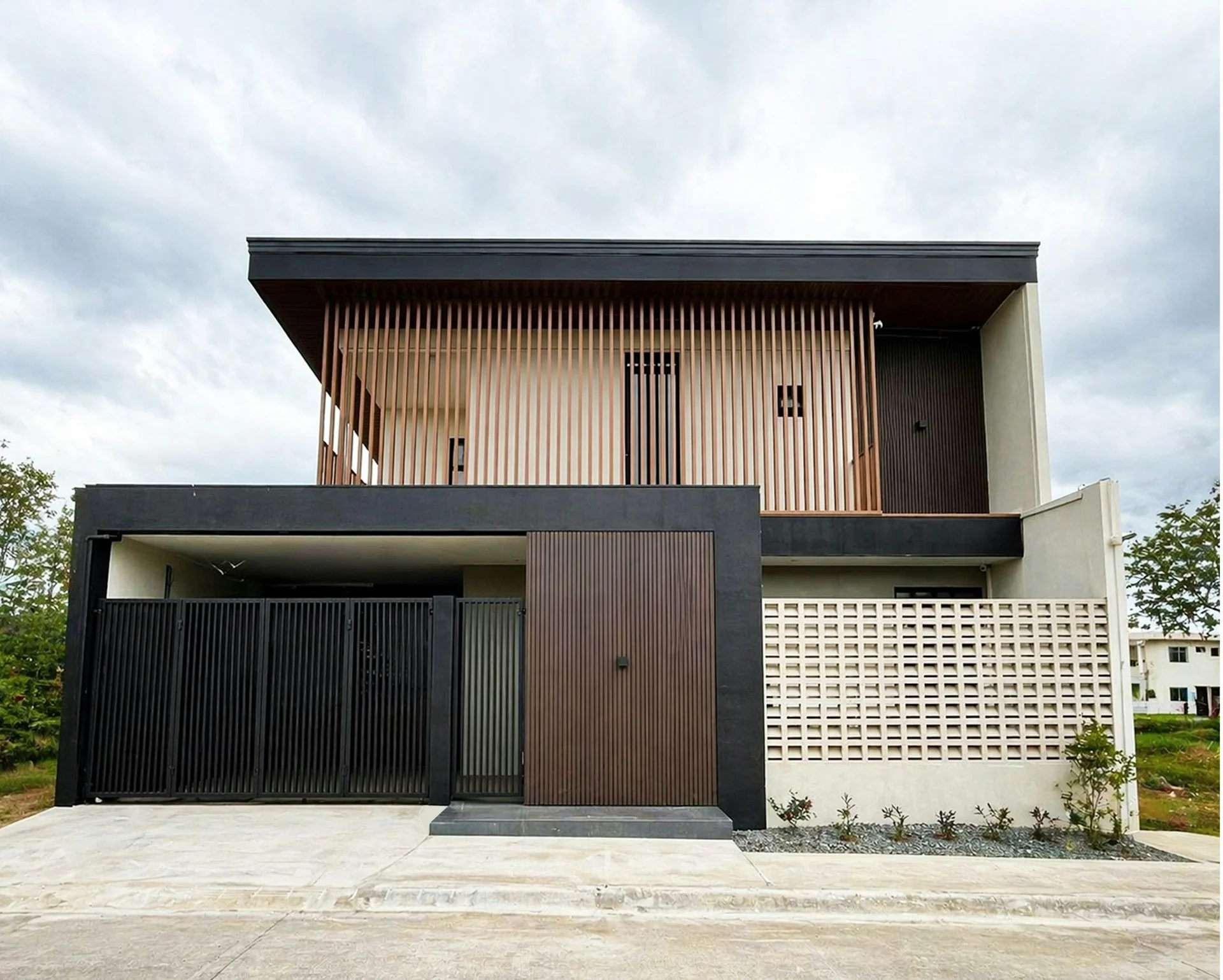 Rumah dua lantai bergaya tropis modern dengan dinding roster beton dan kisi kayu vertikal