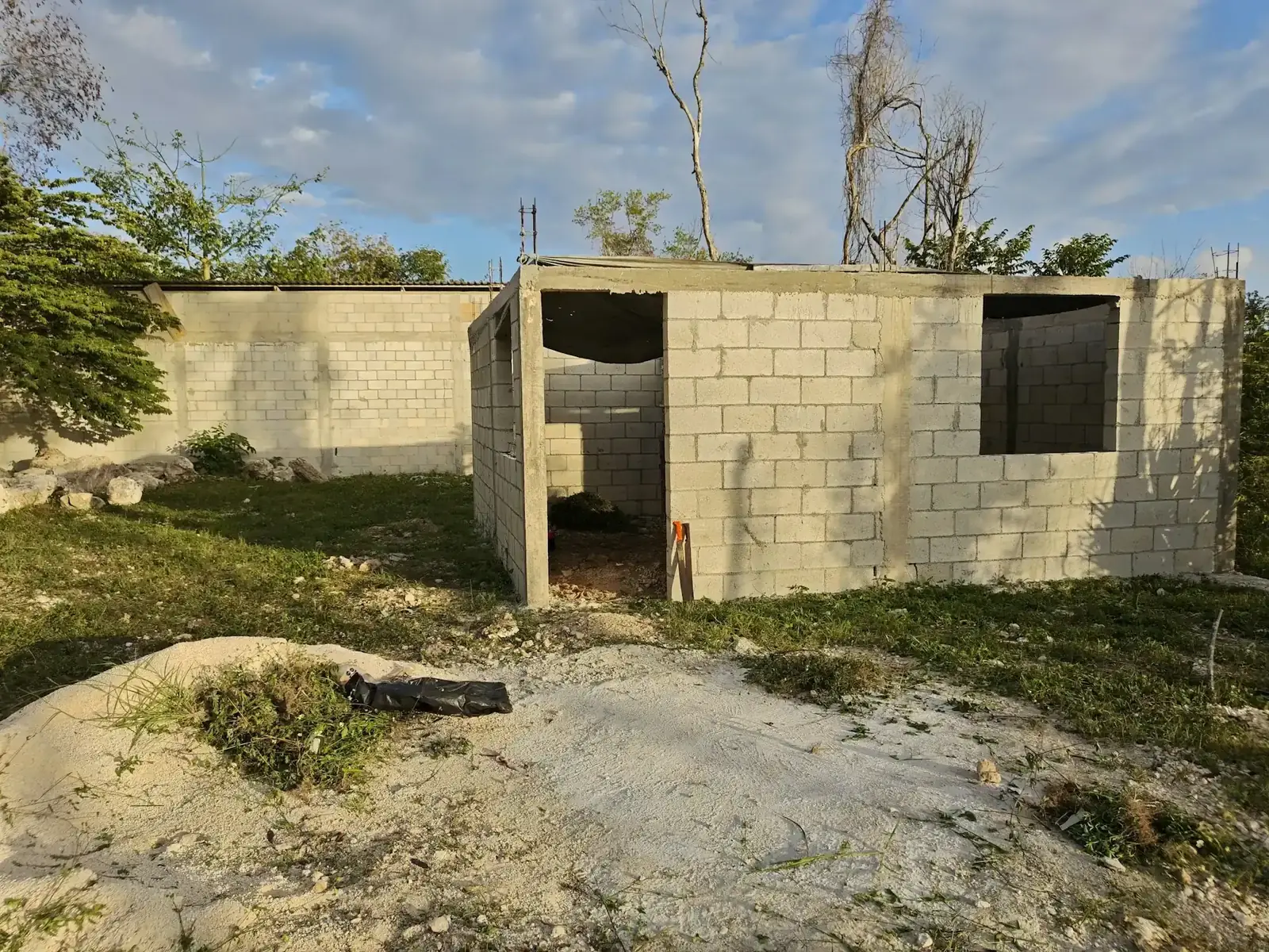 Rumah satu lantai berdinding batako yang belum selesai dibangun, tanpa atap, di halaman berumput