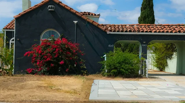 rumah satu lantai beratap genteng dengan carport beratap dan taman depan berbunga bugenvil