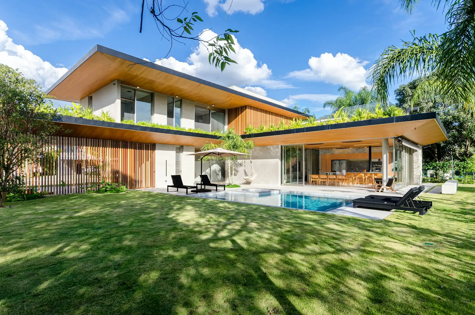 Rumah tropis modern dua lantai dengan atap landai dan overstek lebar berplafon kayu