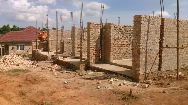rumah bata yang sedang dibangun dengan besi kolom mencuat di atas dinding