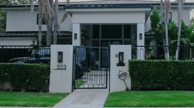 Taman depan rumah modern dengan rumput hijau, pagar tanaman pangkas, dan pohon palem
