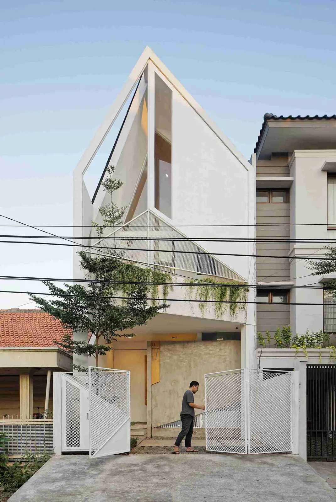 fasad TROW House yang ramping dengan atap segitiga dan tanaman di balkon