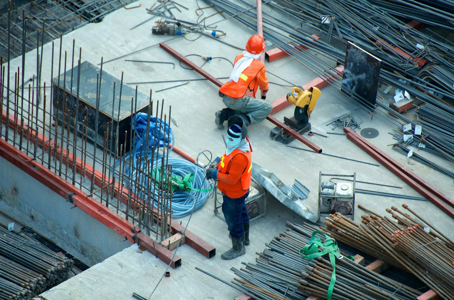 Dua pekerja menyiapkan besi tulangan di atas plat beton dengan stek kolom dan tumpukan besi