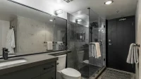 Kamar mandi dengan bilik shower kaca di samping kloset duduk dan meja wastafel