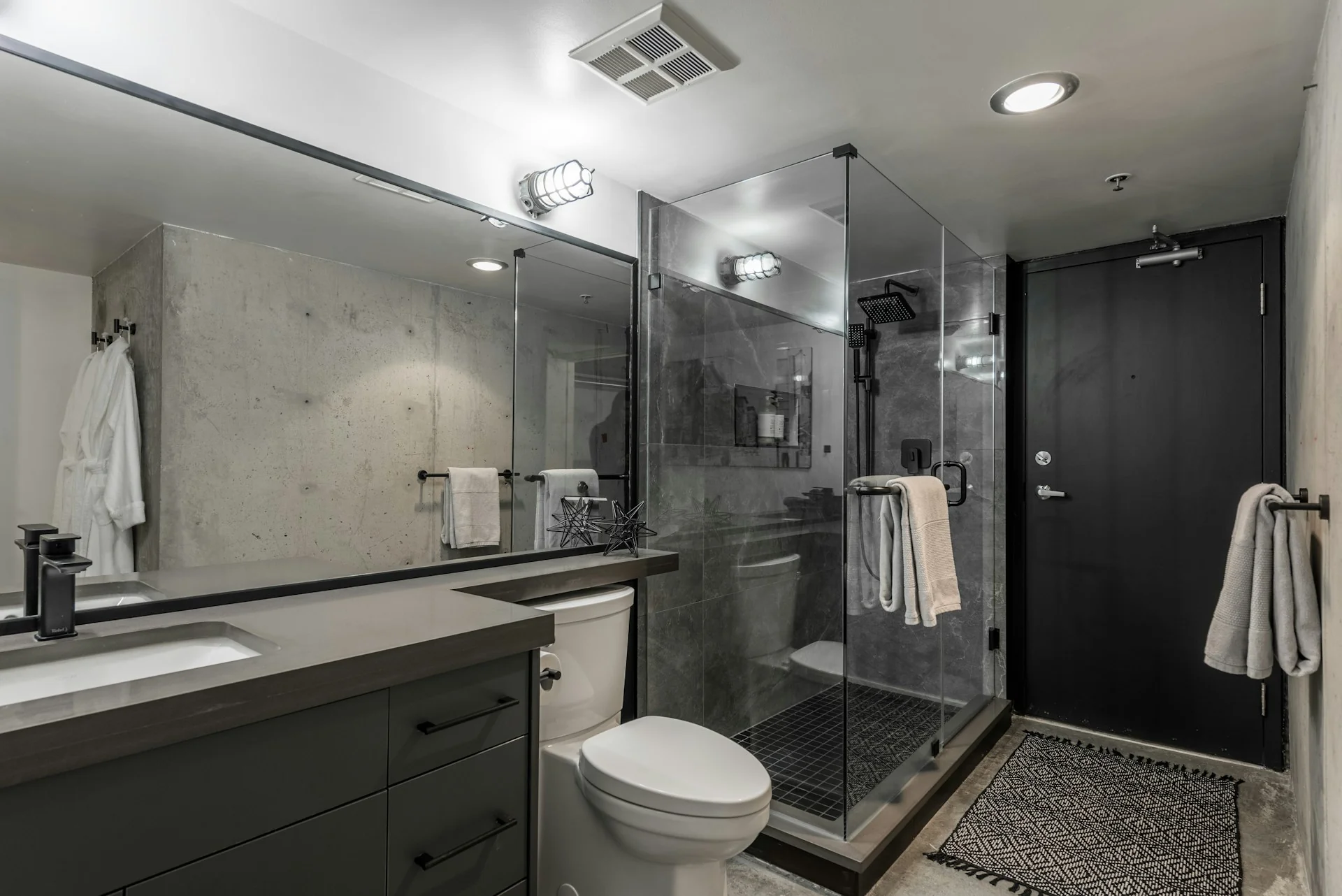 Kamar mandi dengan bilik shower kaca di samping kloset duduk dan meja wastafel