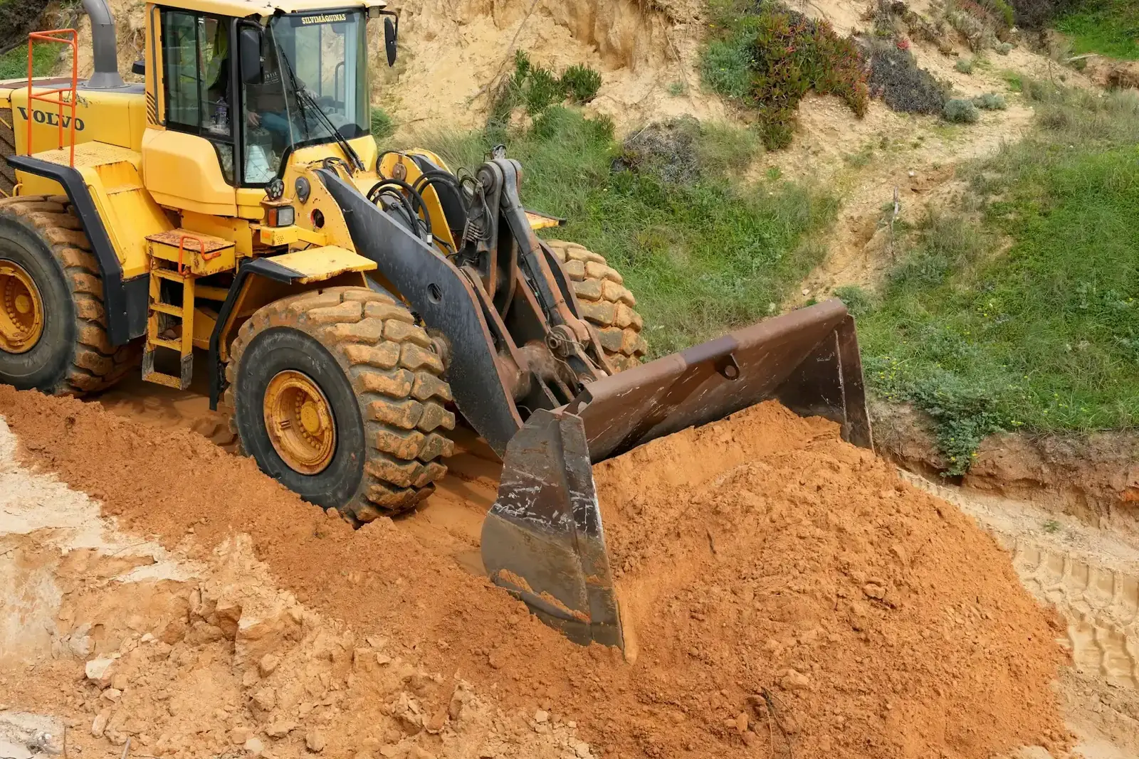 Wheel loader kuning mendorong tumpukan tanah berpasir dengan bucket di lokasi proyek